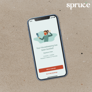 Phone with Spruce scheduled cleaning booking success app screen laying on top of sand with Spruce logo in top right corner.