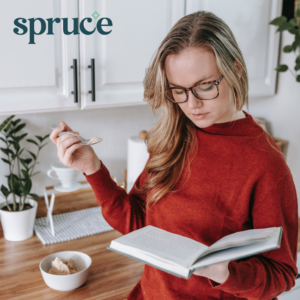 A woman in a red sweater reading a book and drinking a warm drink. The Spruce logo is in the top left corner.